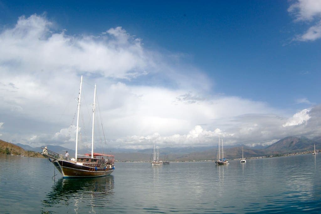 Su Perisi — Gulet anchored in a calm bay with sailing yachts beyond